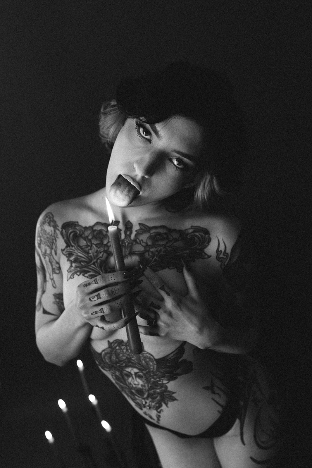 A black and white photo of a girl holding a candle to her tongue in a boudoir photoshoot