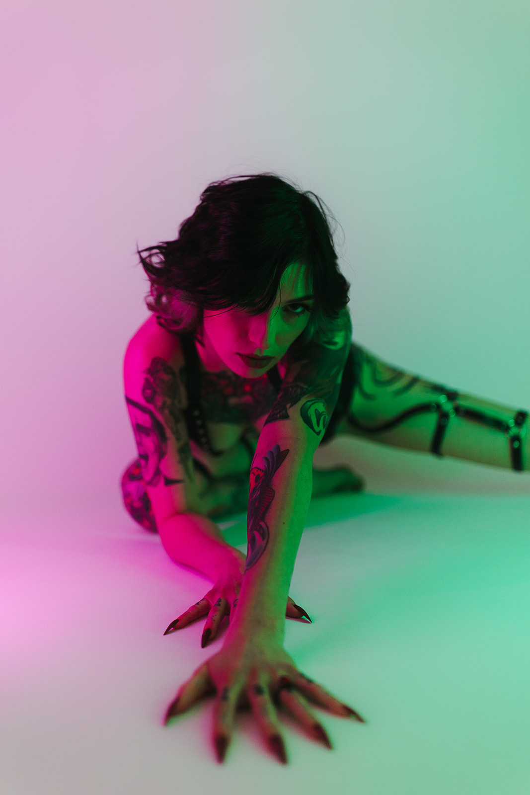 Different colored lighting hitting a girl posing for boudoir photos with her hands reaching towards the camera