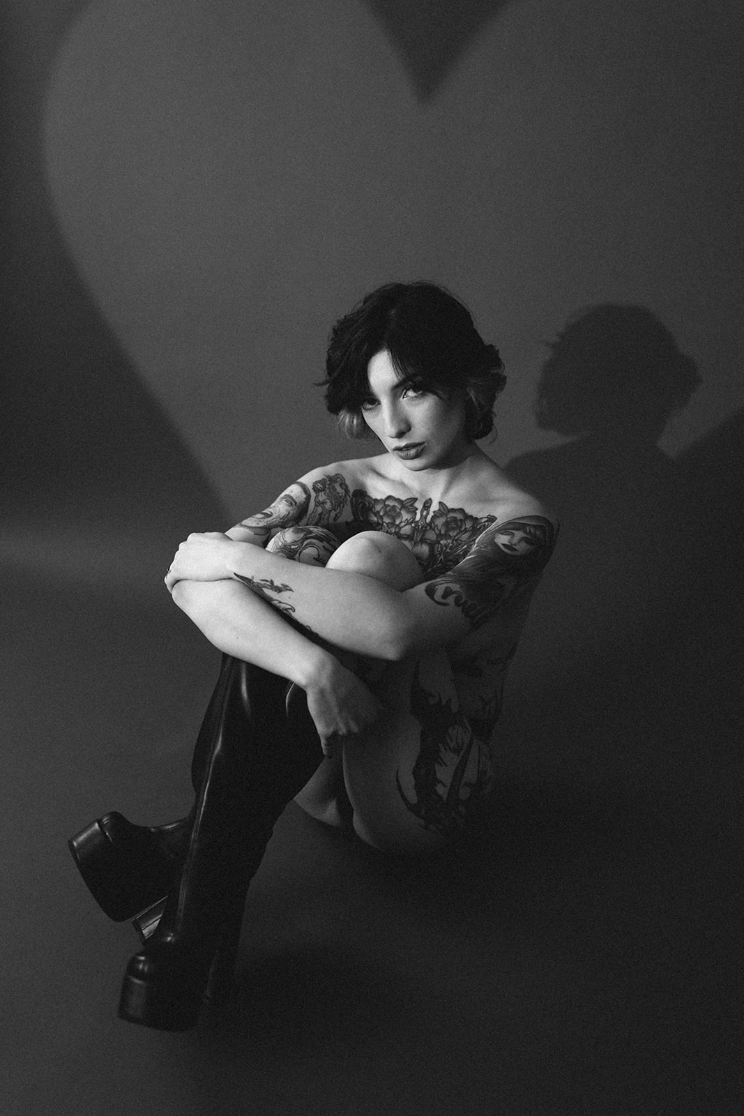 A black and white photo as a boudoir photoshoot idea, with a girl sitting on the ground in black go-go boots