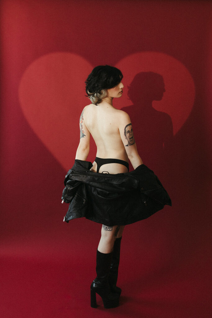 A girl holding her leather jacket down, exposing her back for boudoir photos
