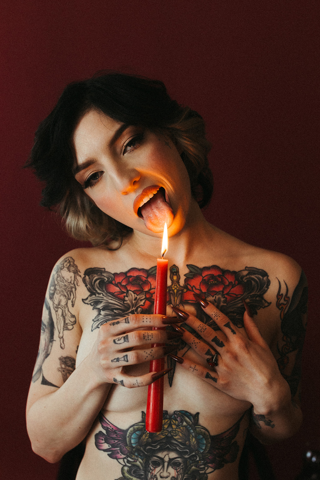 A girl holding a red candle to her tongue as boudoir photoshoot ideas