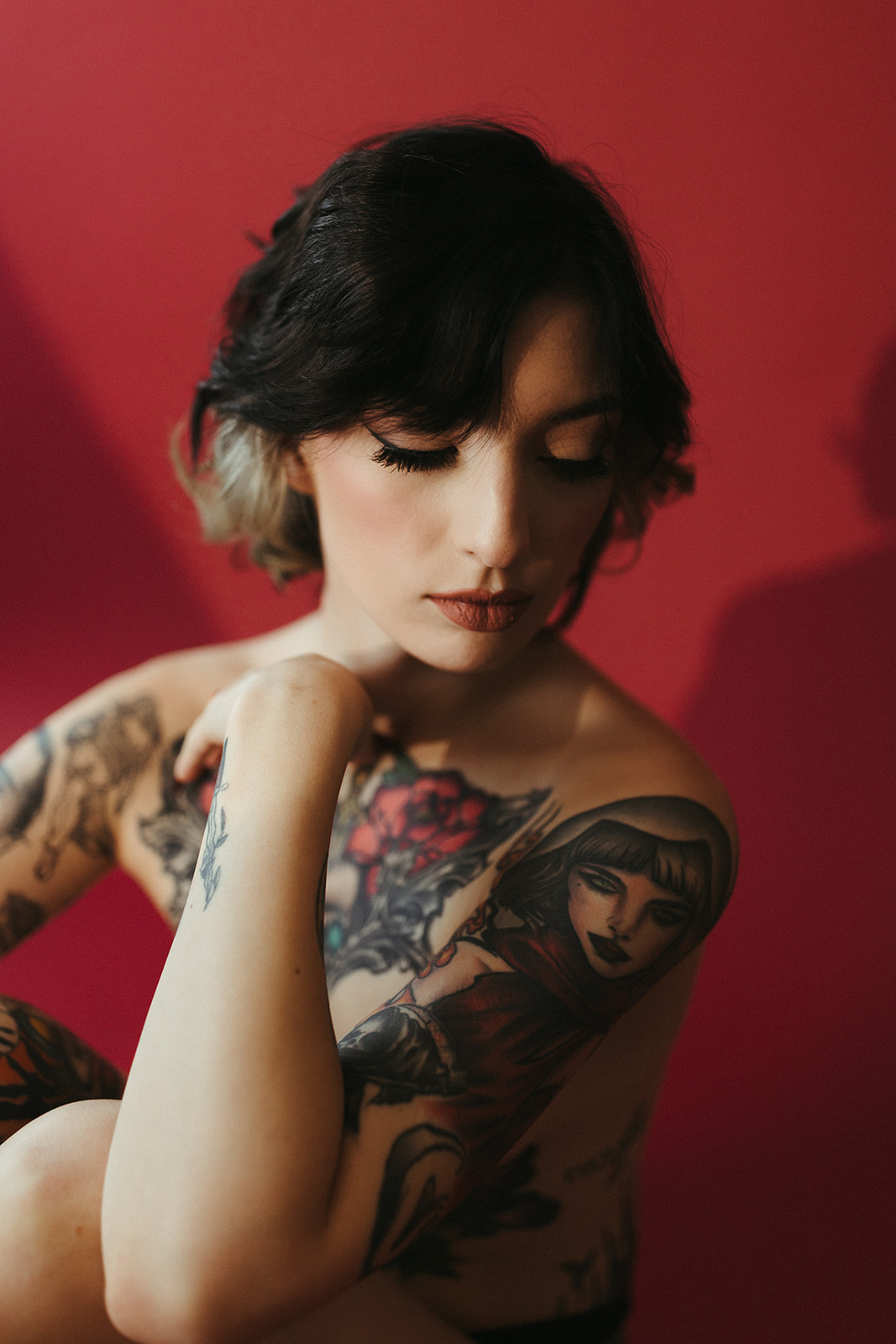 A girl looking down during boudoir photos, showing off her eye makeup and tattoos on her upper arm