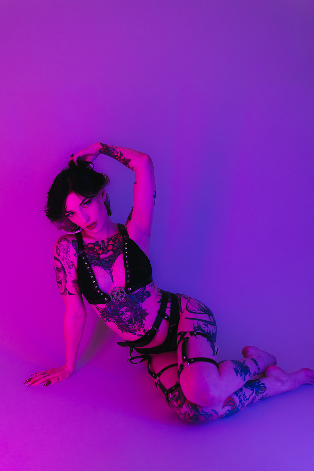 A girl on the ground for boudoir photos in leather lingerie, holding her hair