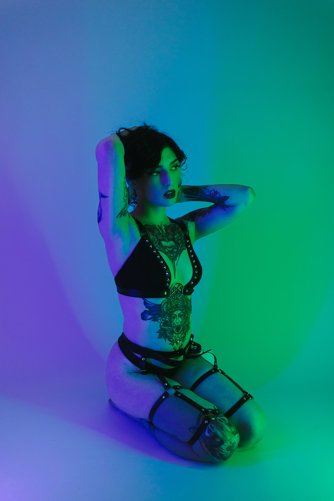 A woman posing for her boudoir photos by sitting on the ground with green and blue lighting hitting her
