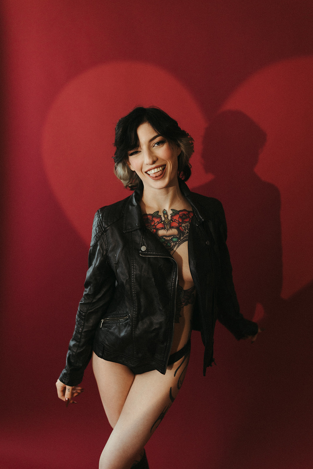 A girl in a leather jacket with a heart-shaped light hitting behind her for boudoir photoshoot ideas