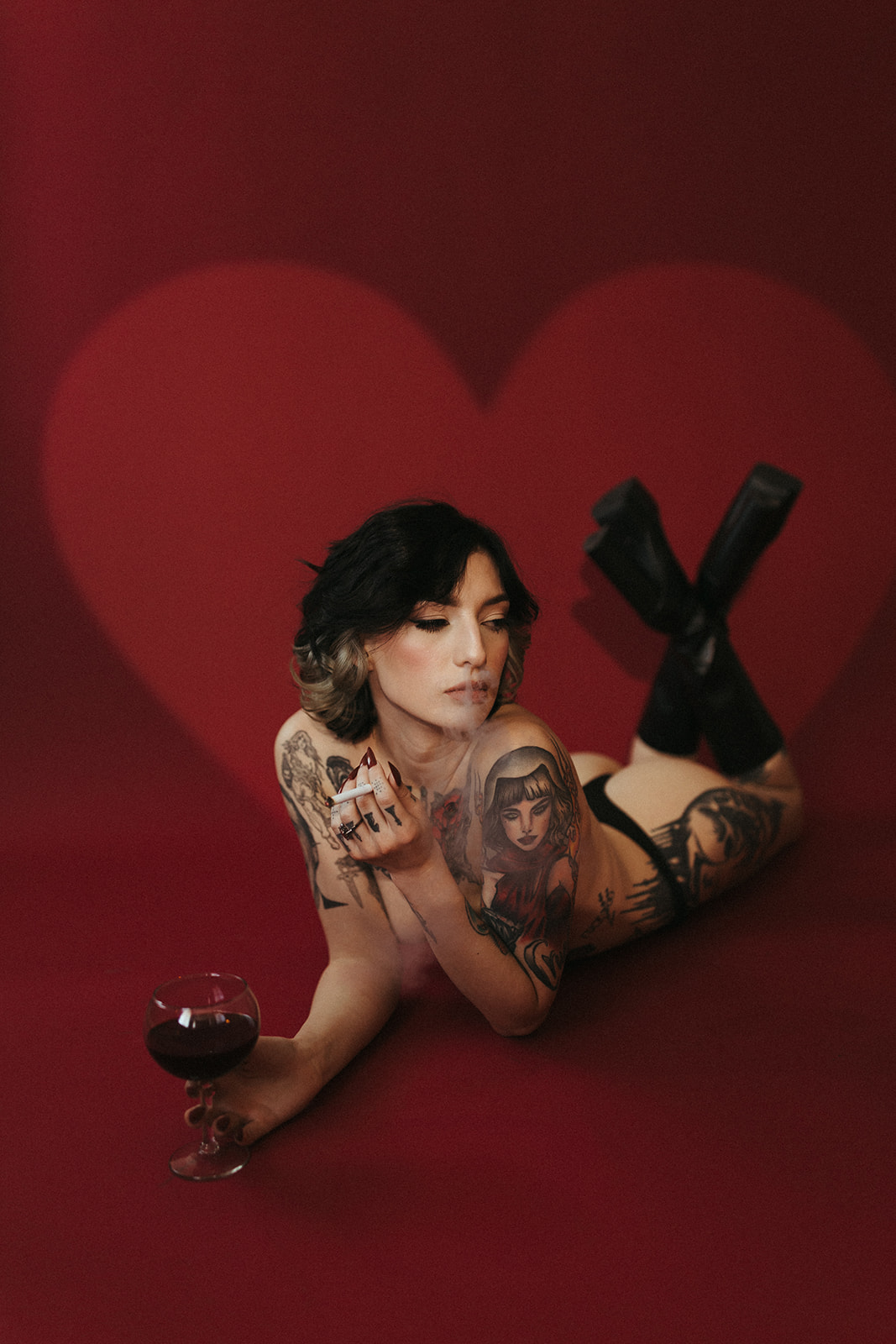 A woman laying on the ground showing boudoir photoshoot ideas: incorporating wine and cigarettes