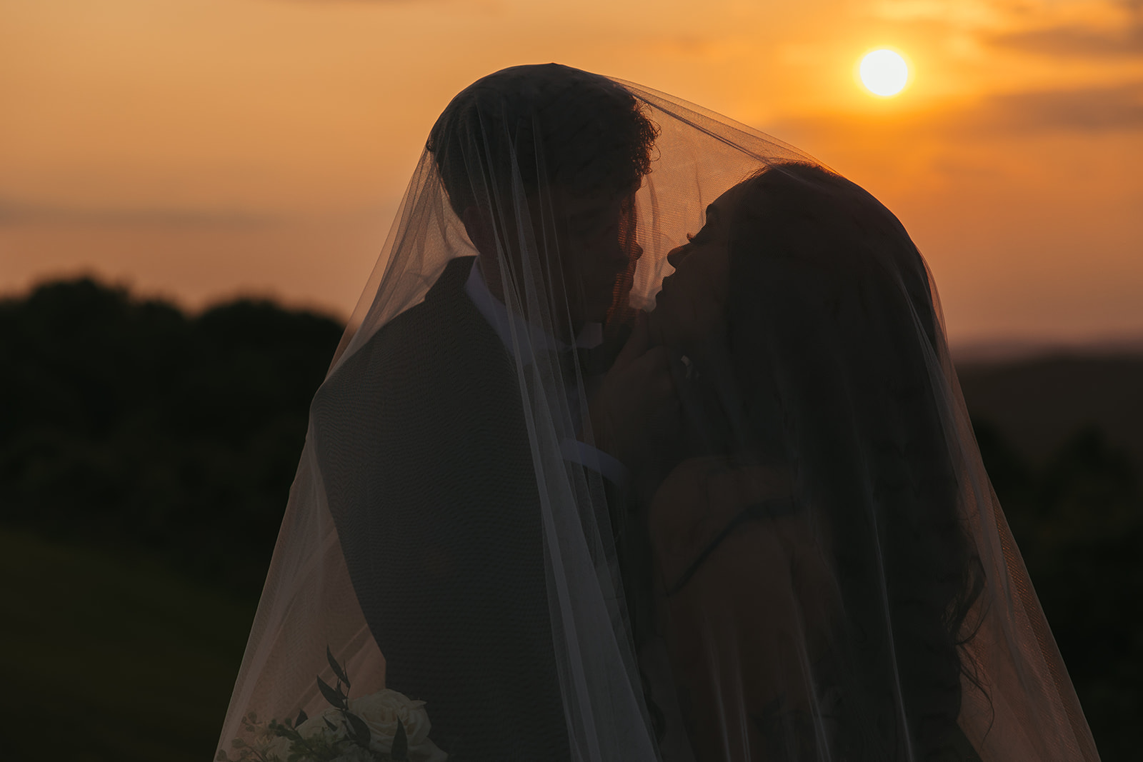 Bride and groom leaning in for a kiss under a veil