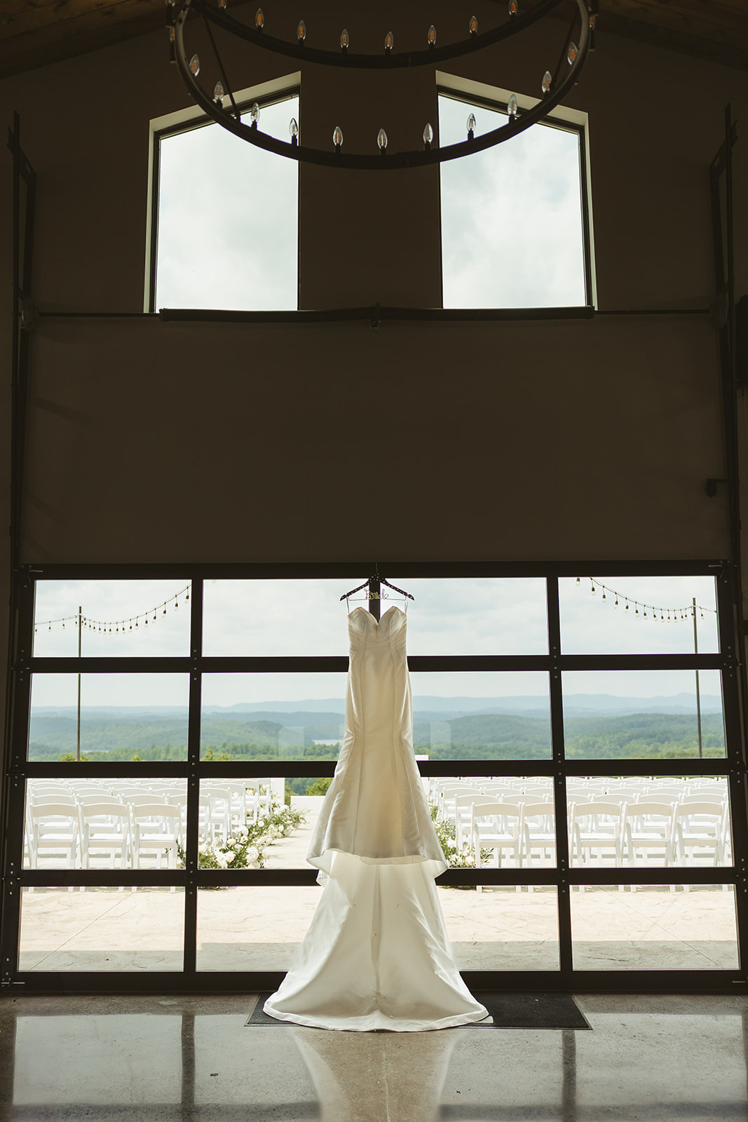 A simple elegant wedding dress hanging up at the venue with mountains in the background