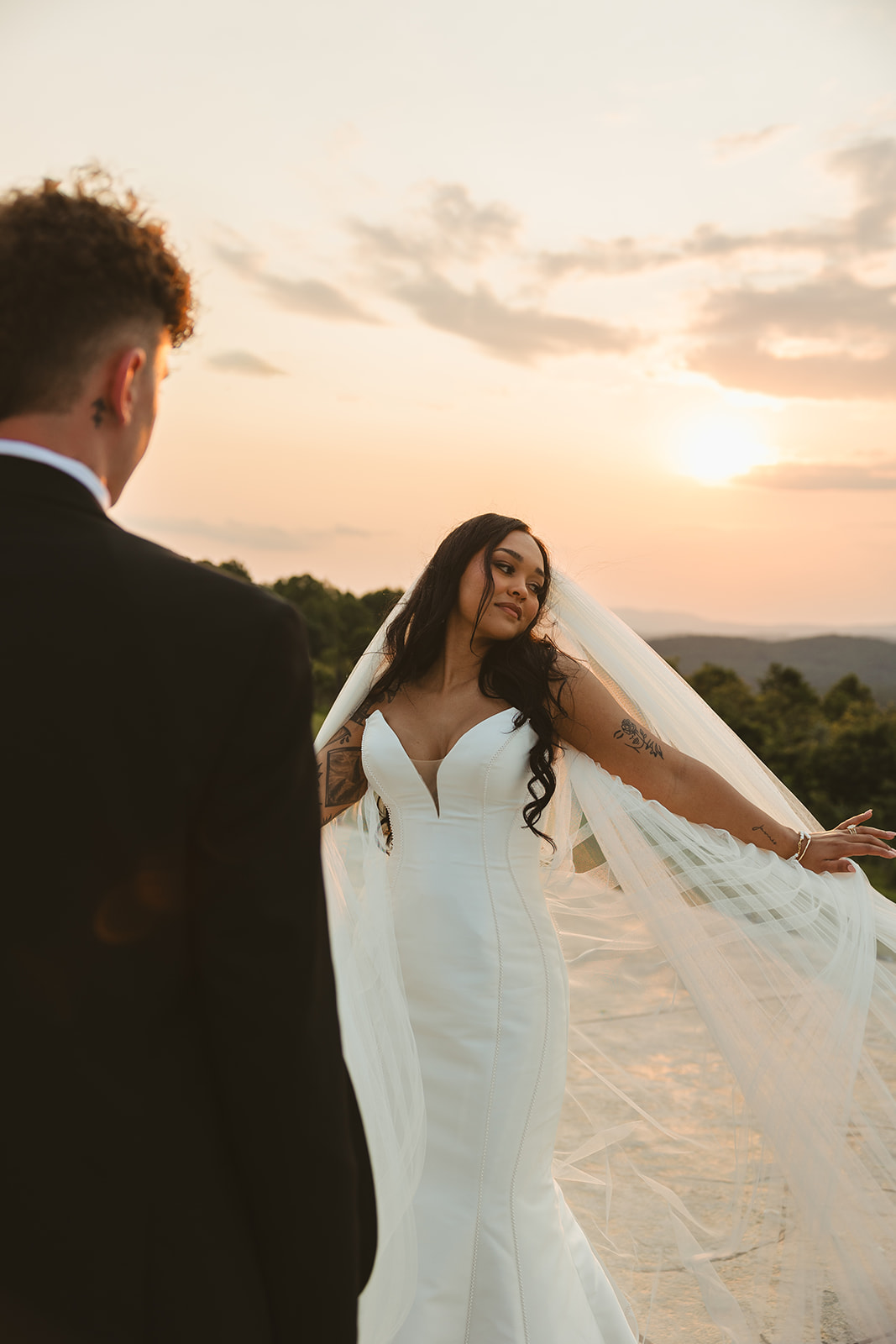 Groom looking at bride holding her veil out during sunset wedding photos