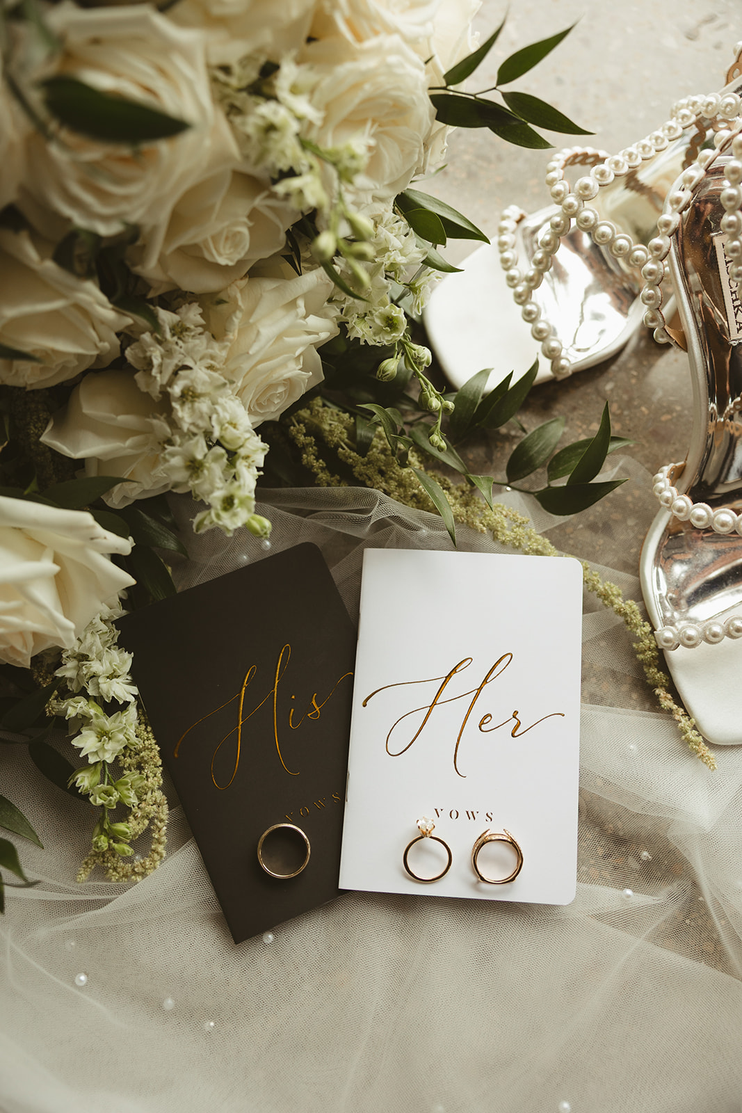 A wedding detail photo of a veil, vow books, wedding shoes, and white wedding flowers
