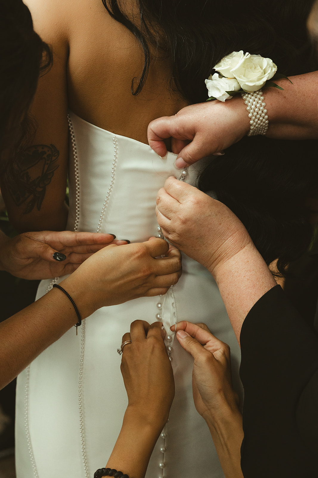 Bride's mother, grandmother, and bridesmaids buttoning her wedding dress