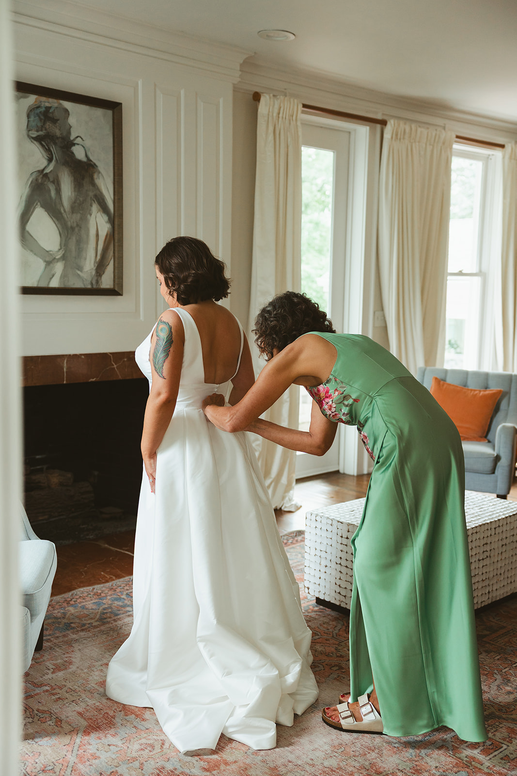 A bride's mother helping her put on her wedding dress