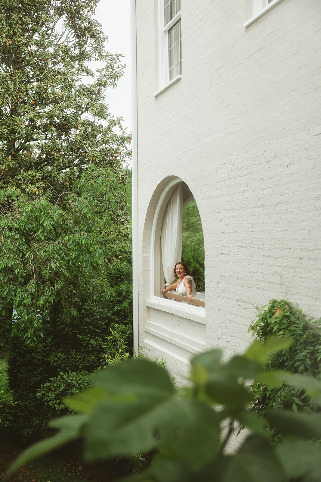 Bridal portrait taken through an arched window on a white brick wall