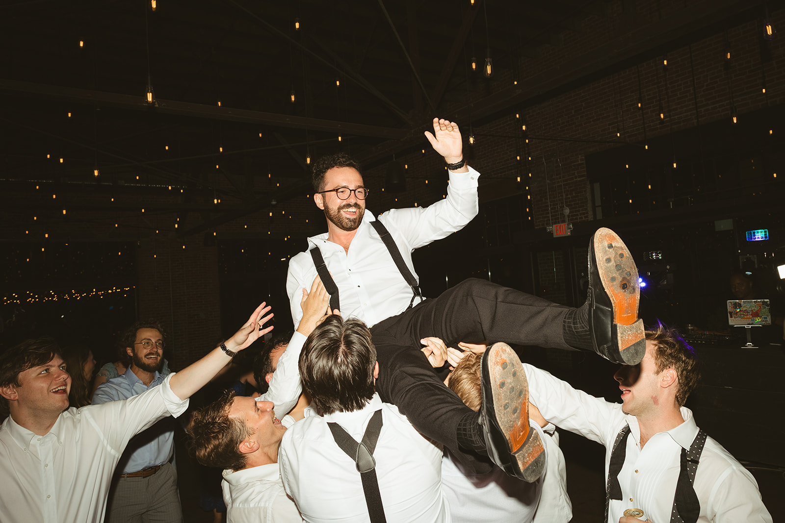 A wedding party lifting a groom in the air during a wedding reception