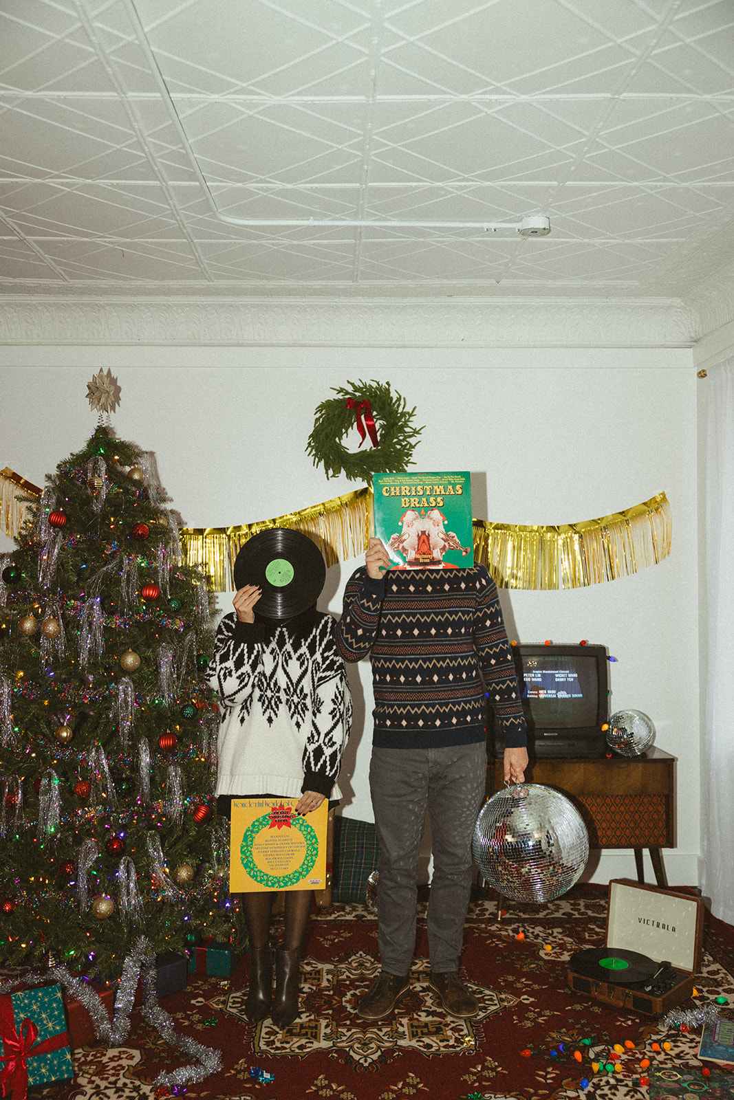 A couple holding parts of a vinyl record in front of their faces during retro Christmas pictures