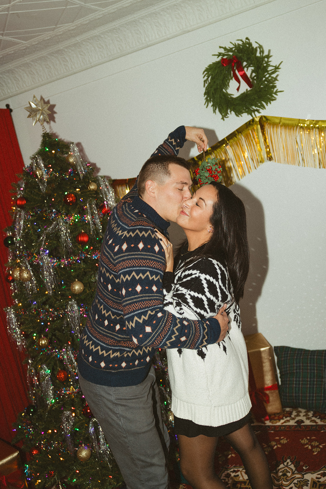 A man holding mistletoe and kissing his partner underneath it