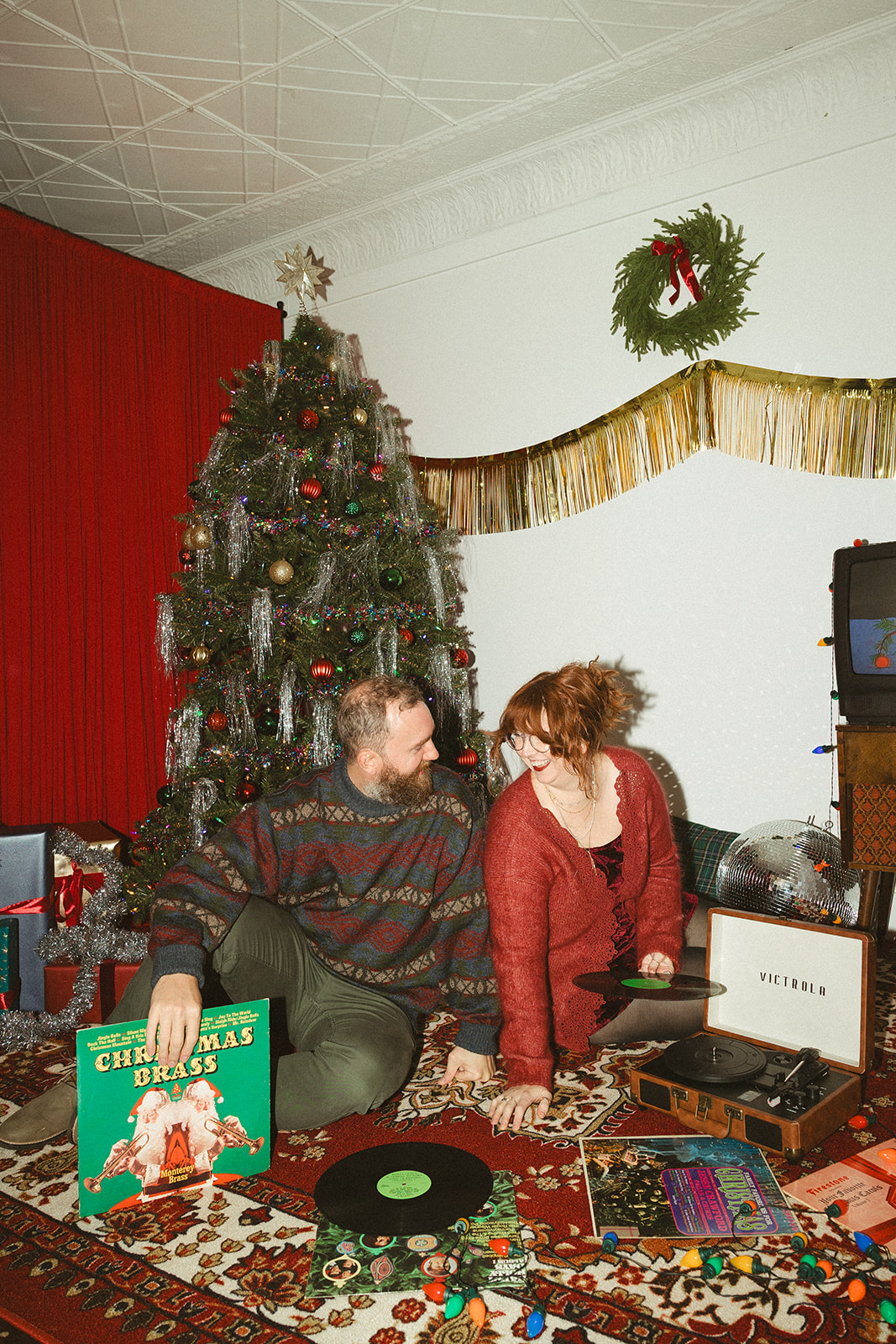 A couple sitting in front of a christmas tree for retro christmas pictures