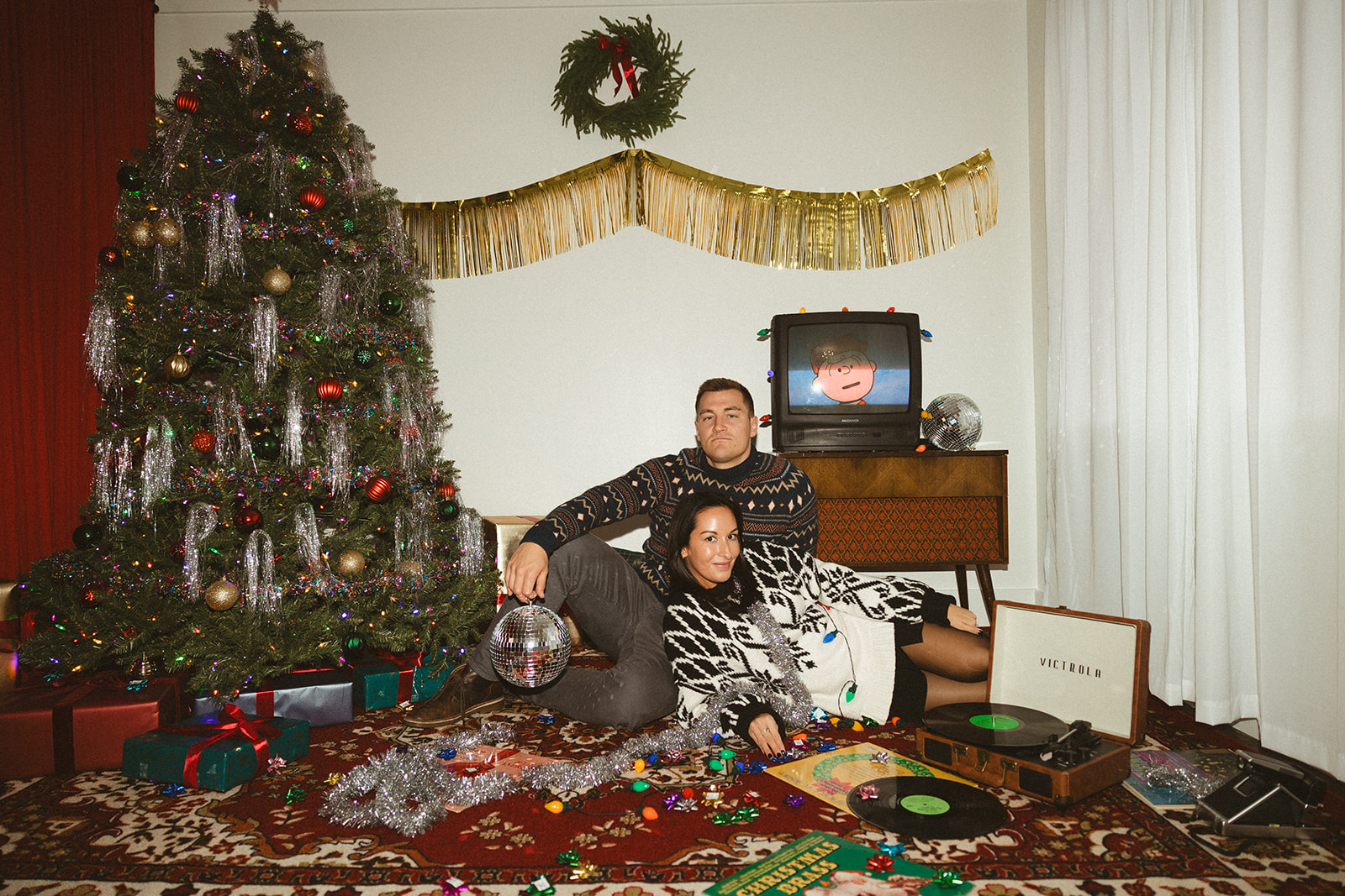 A couple laying on the ground with disco balls and vinyl records for retro christmas pictures