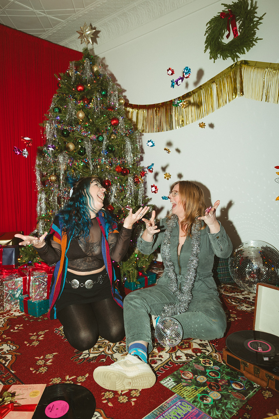 A couple throwing present bows up in the air in front of a Christmas tree for retro christmas pictures