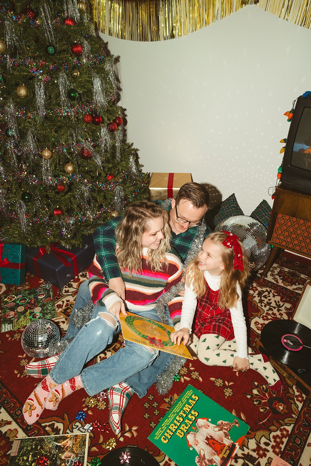 A family reading a Christmas book in front of a Christmas tree