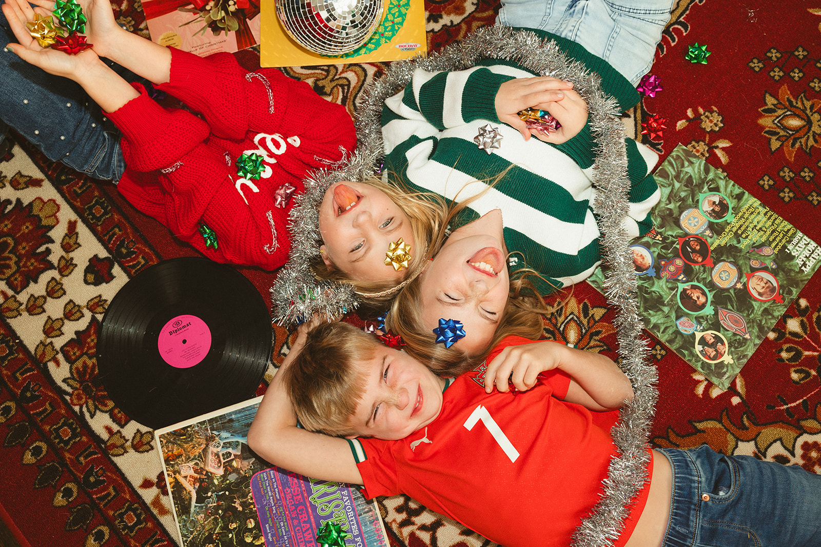 Three kids laying on the ground with present stickers, tinsel garlands, adnd vinyl records