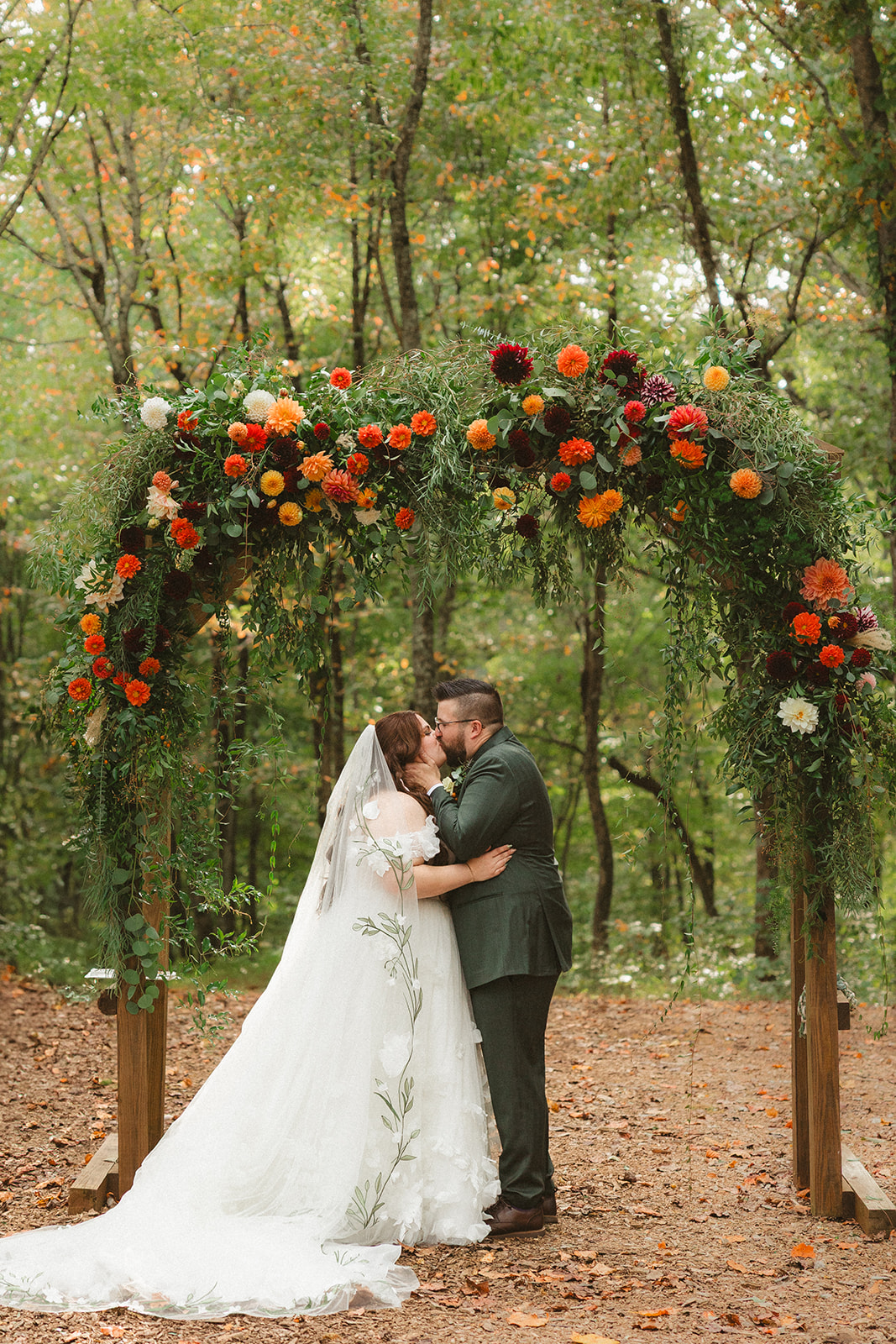 A bride and groom kissing under a wedding ceremony arch in the woods at Ancient Lore Village