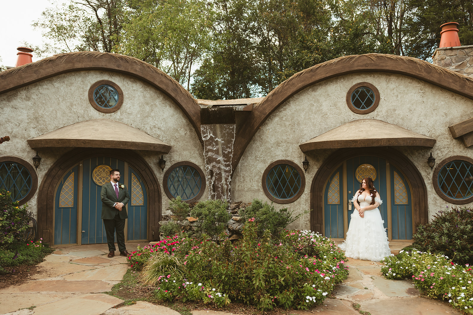 A bride and groom standing in front of hobbit houses at ancient lore village