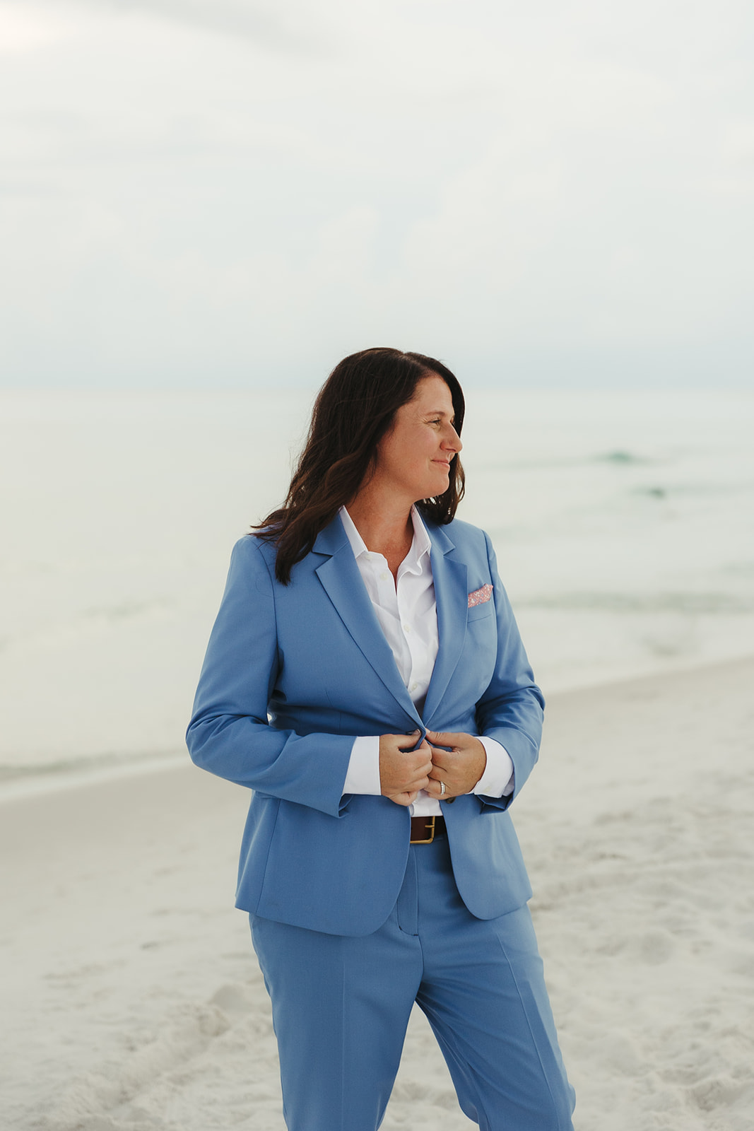 A bride buttoning up her suit on the beach in 30a