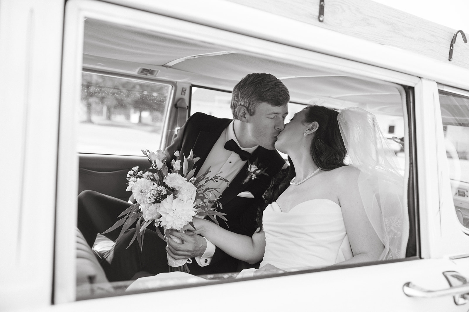 A bride and groom kissing in a wedding getaway car