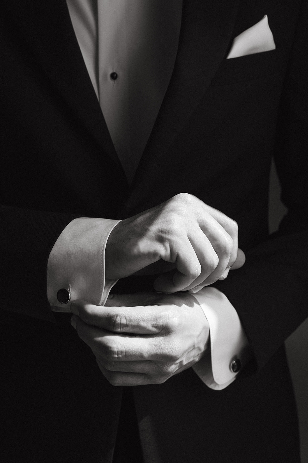 A groom buttoning his cuffs before his wedding