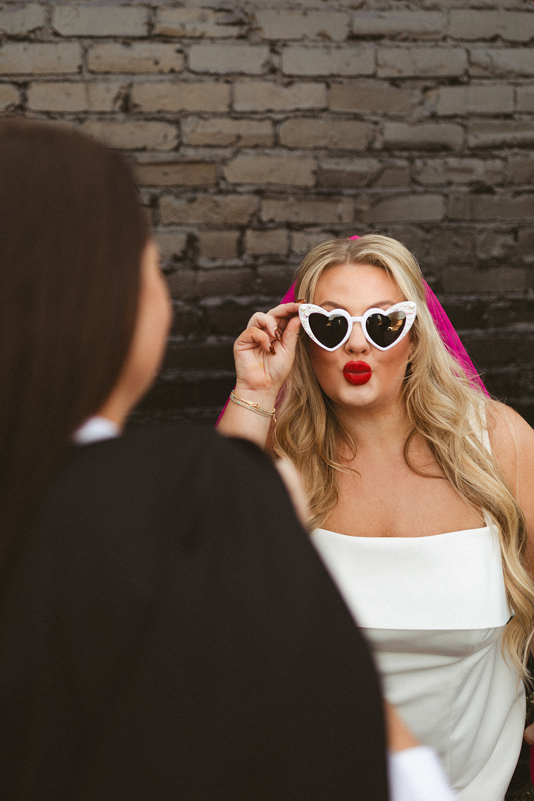 Two brides posing for elopement photos in front of a black brick wall