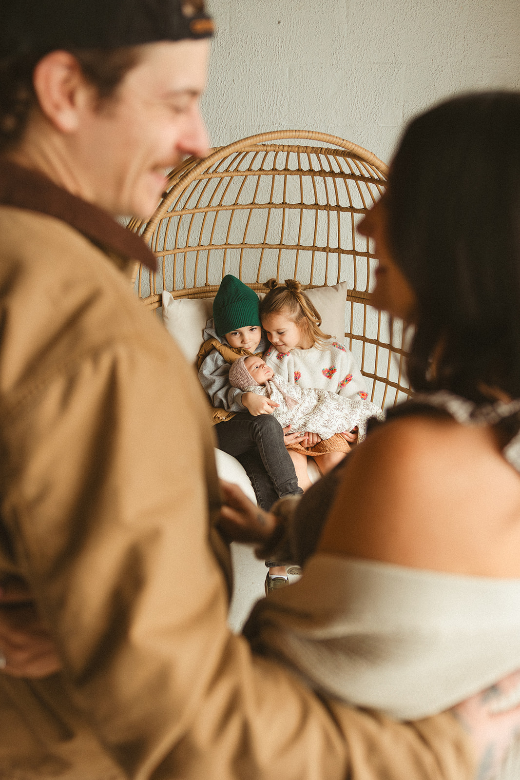 A mom and dad watching Two siblings holding their newborn baby sister